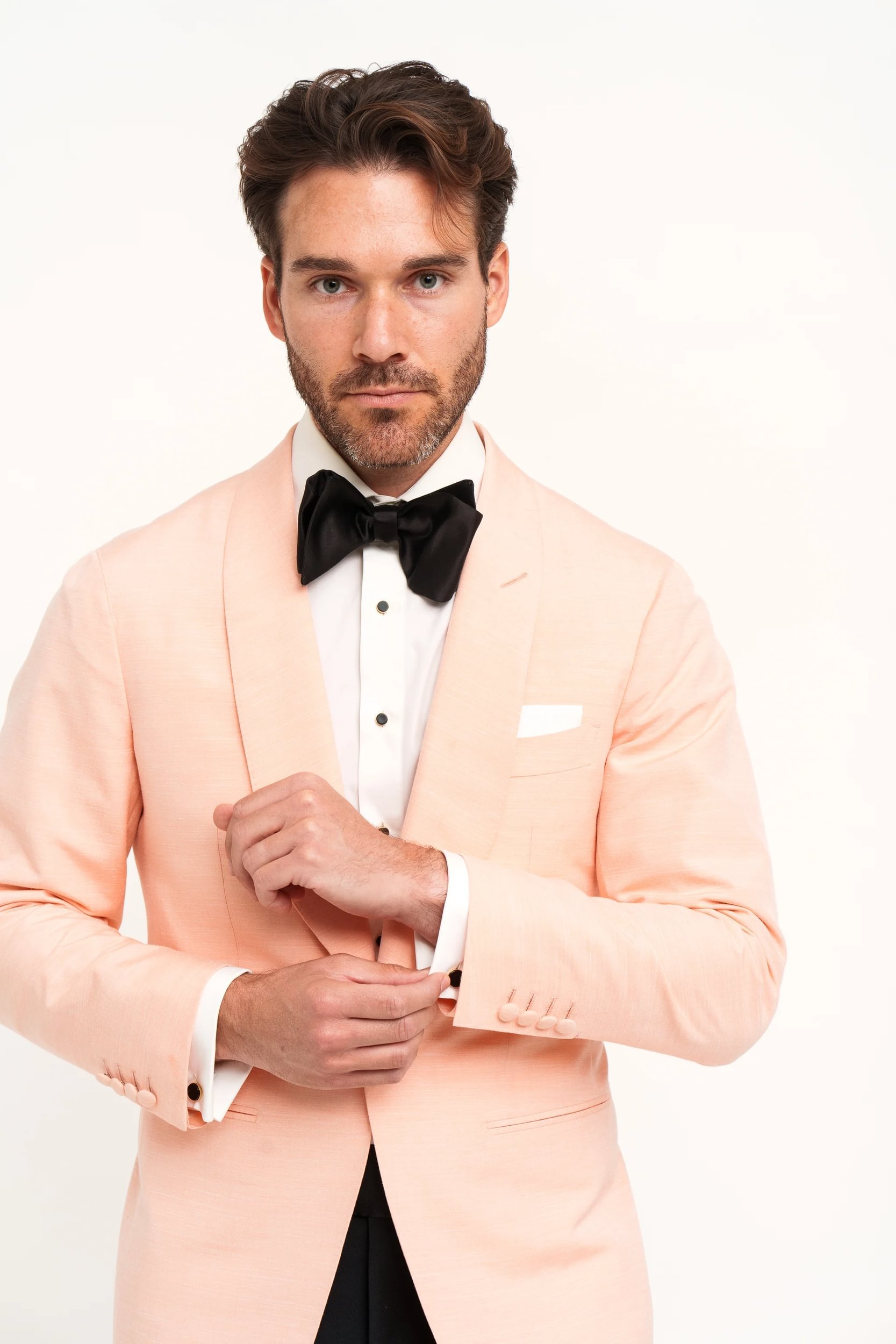 Man in peach suit with black bow tie fixing cufflinks
