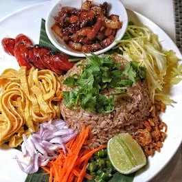 Thai fried rice dish with shrimp paste, garnished with various ingredients like egg strips, sausage, onions, carrots, lime, and cilantro.