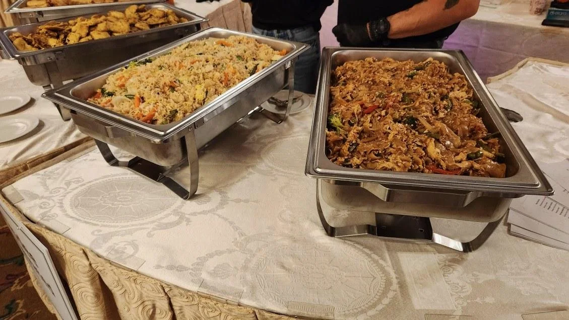 Buffet catering trays with stir-fried noodles, fried rice, and fried snacks on a tablecloth.