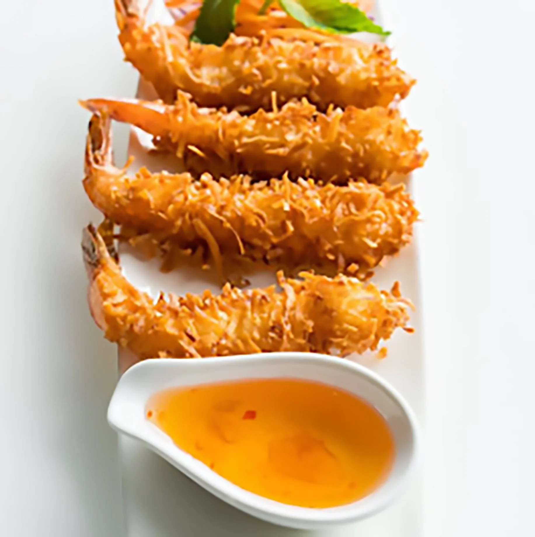 Four coconut shrimp on a white plate with a small dish of dipping sauce.
