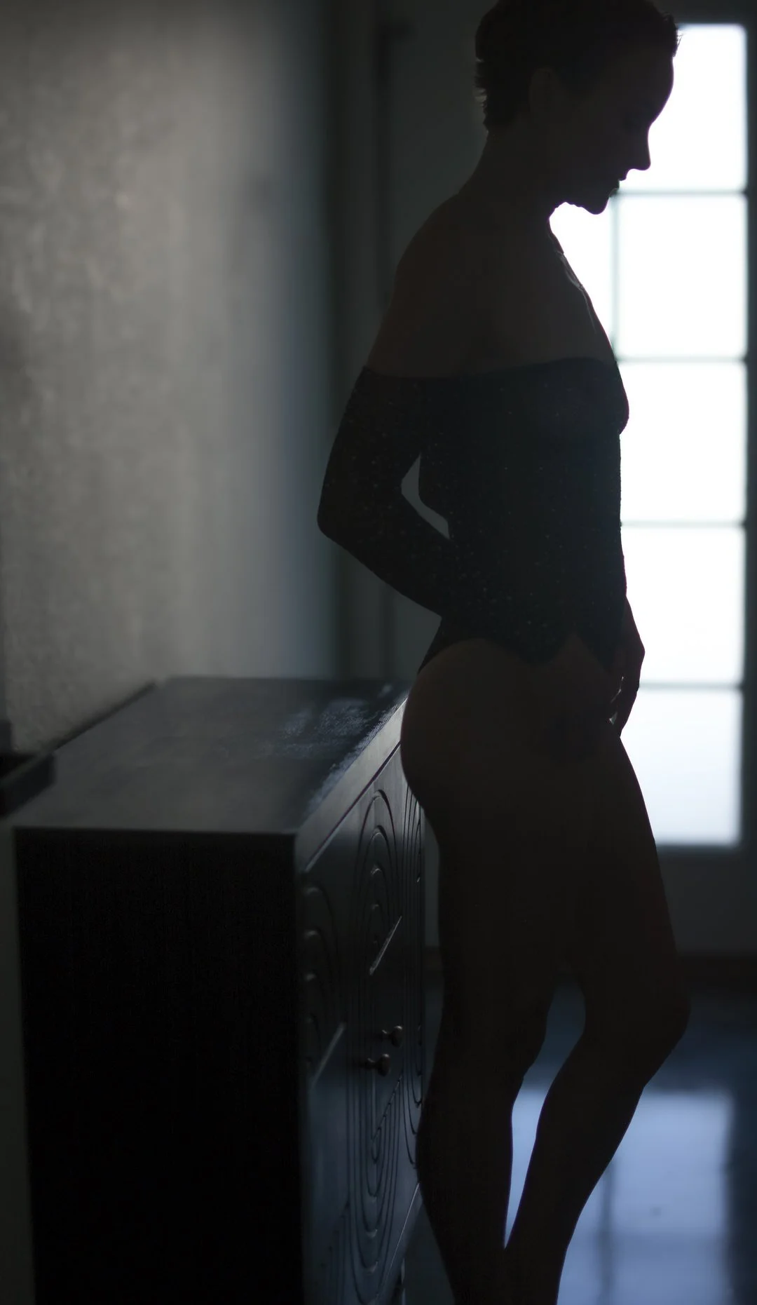 Woman with a shaved head standing in window light during a strength and healing portrait session by Rebekah Ayantola in Tucson, Arizona.