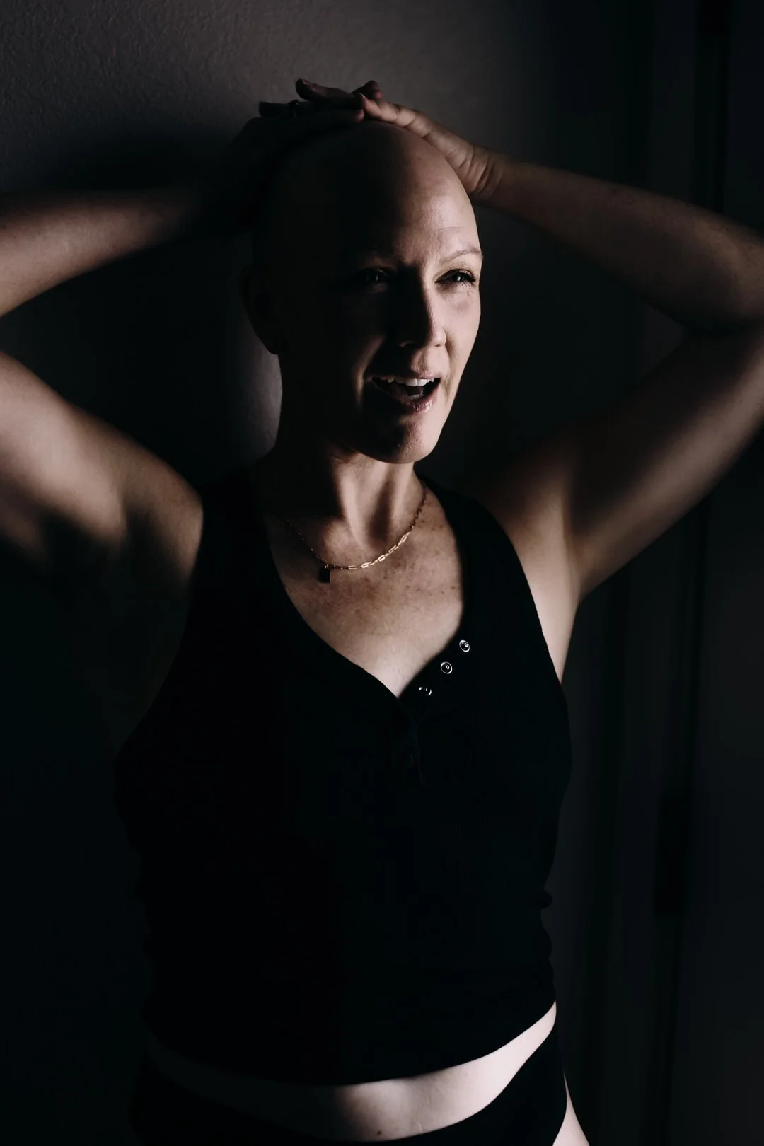 woman with cancer lifting her arms in soft studio light during a fine art portrait session, expressing strength, confidence, and resilience