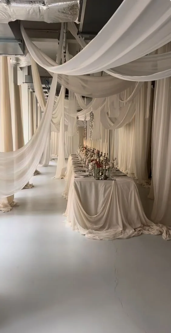 Elegantly decorated table with white drapes and candles in a reception hall.