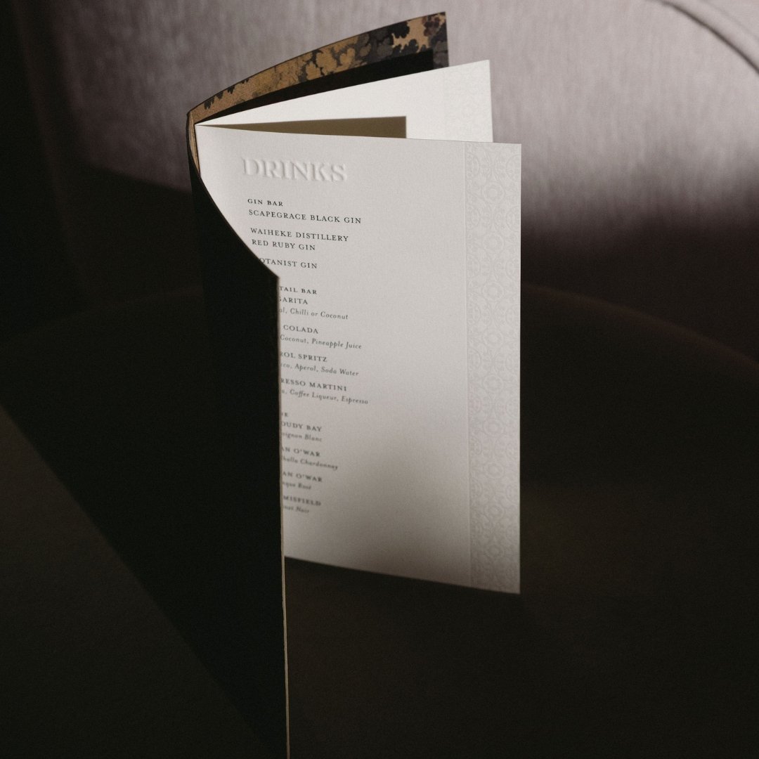 Angela and Justin’s wedding drinks menu with embossed heading, subtle patterned detail and layered paper construction.