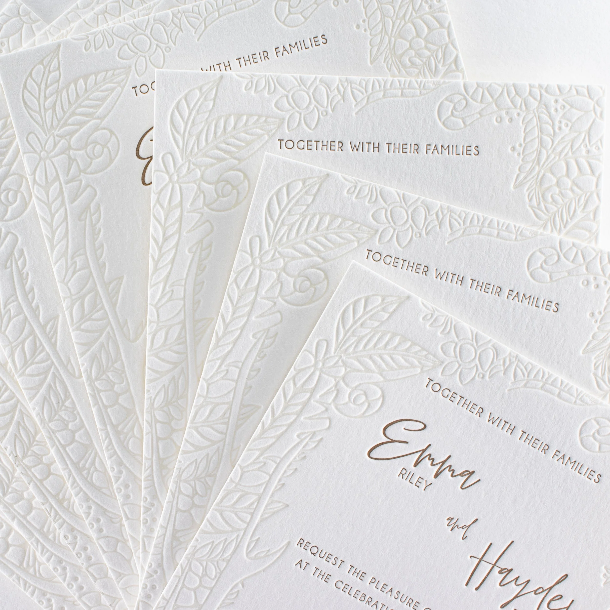 Close-up of Emma and Hayden’s wedding invitations showing the deeply impressed letterpress floral border and warm gold typography.