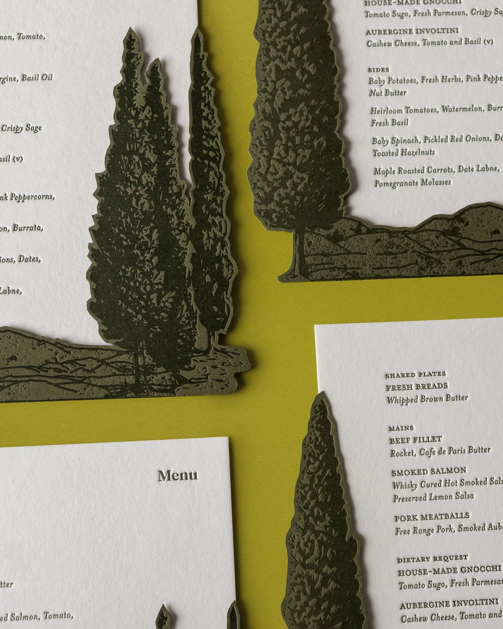 Close-up of Greer and Cohen’s wedding menus featuring die-cut letterpress conifers layered over textured cotton card.