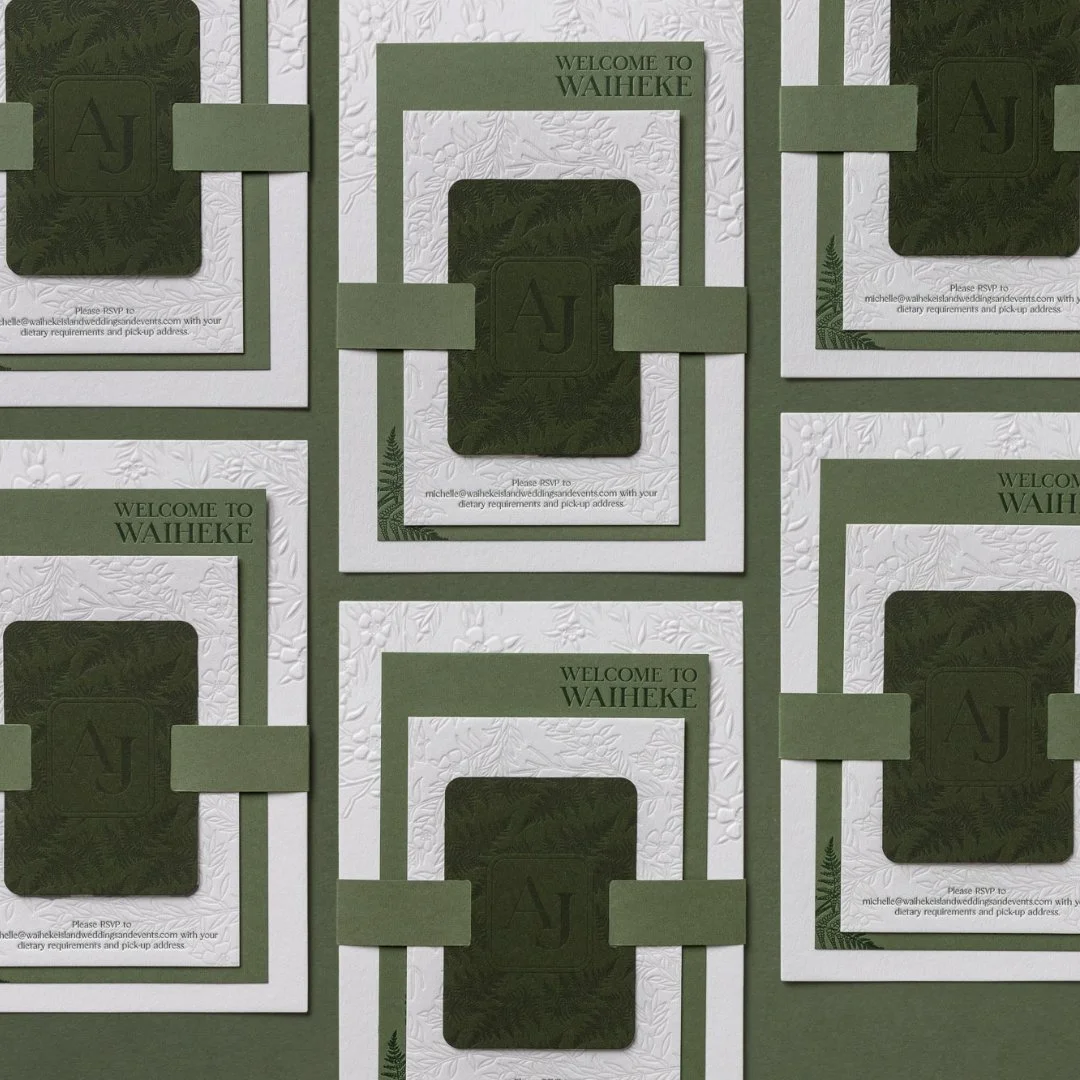 Layered green and cream wedding invitations with embossed mānuka and deep green monogrammed invitation ties.