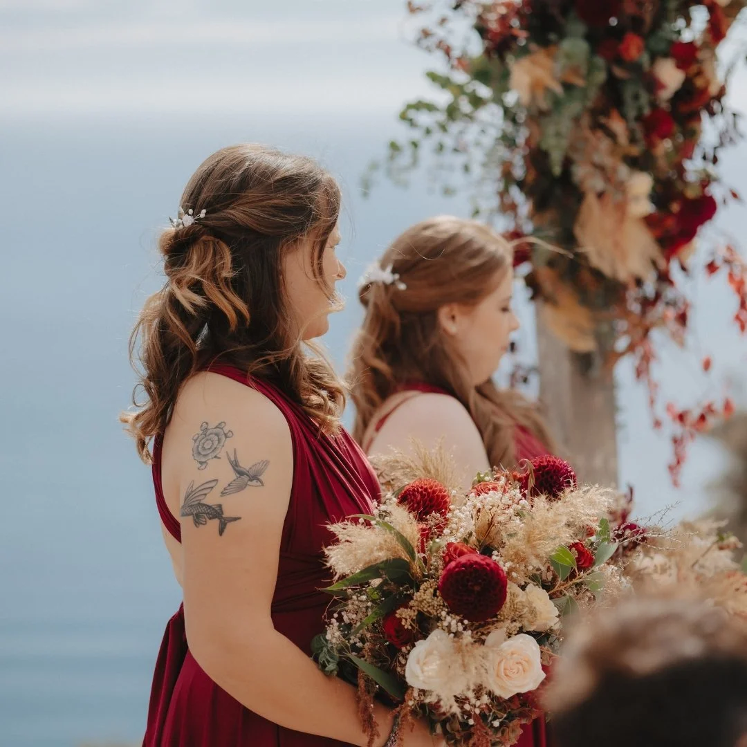 Bridesmaids at Brontë and Simon’s Boomrock wedding in burgundy dresses, carrying bouquets of deep red and cream flowers with dried grasses.