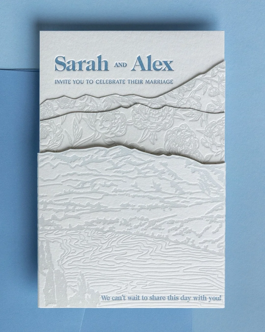 Layered letterpress wedding invitation with die-cut Coronet Peak landscape and tonal deboss peonies on thick cotton paper.
