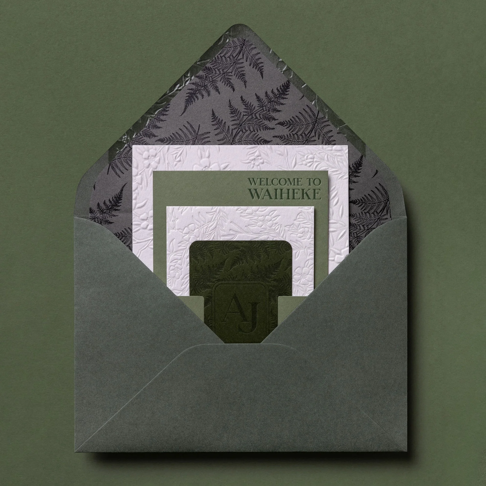 Green wedding envelope opened to reveal a fern-patterned liner and layered cream and green invitation suite.