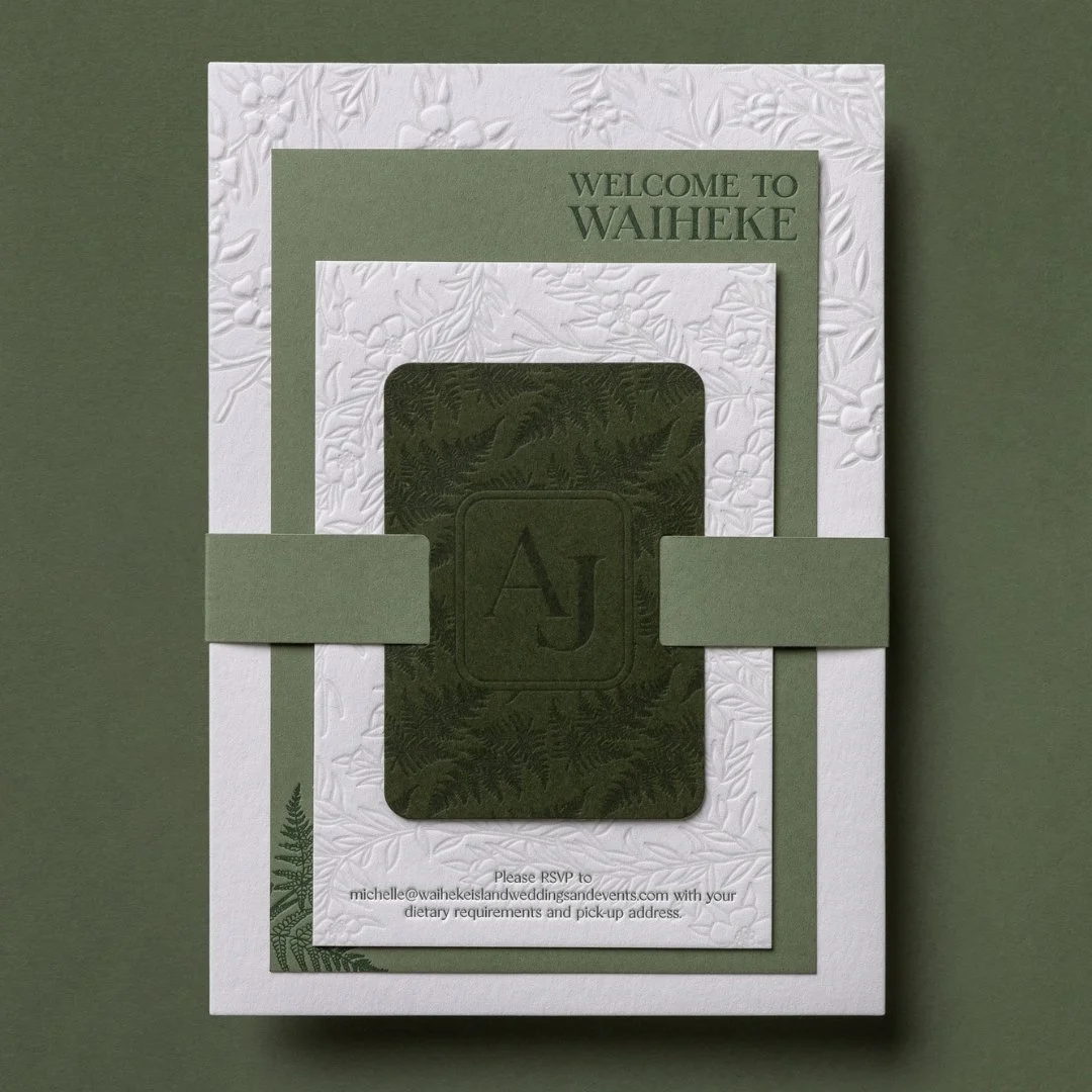 Layered green and cream wedding invitation with deep-green monogrammed invitation tie and embossed botanical details.