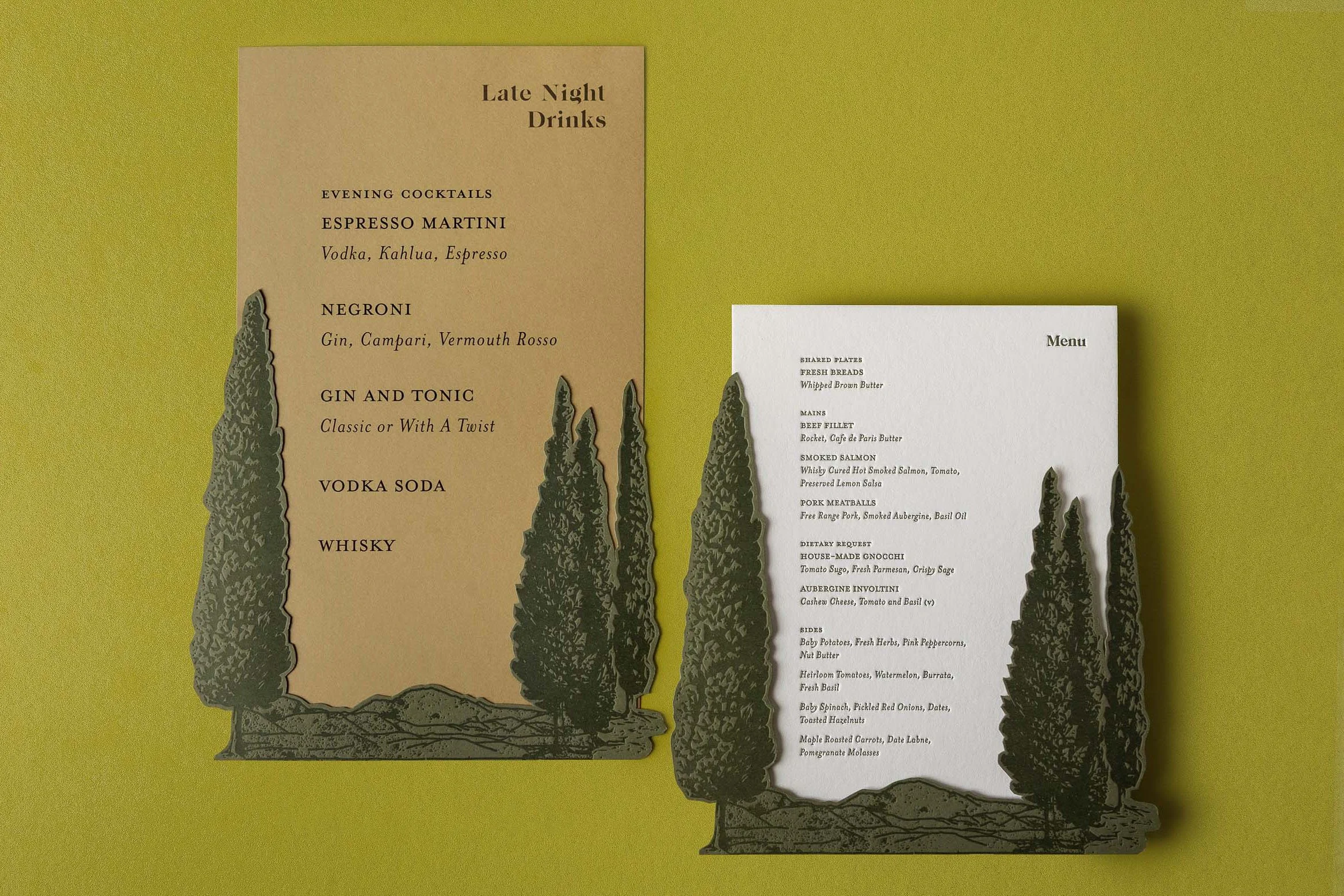 Greer and Cohen’s wedding dinner and late-night drinks menus featuring layered die-cut conifers and Mount Starveall artwork.