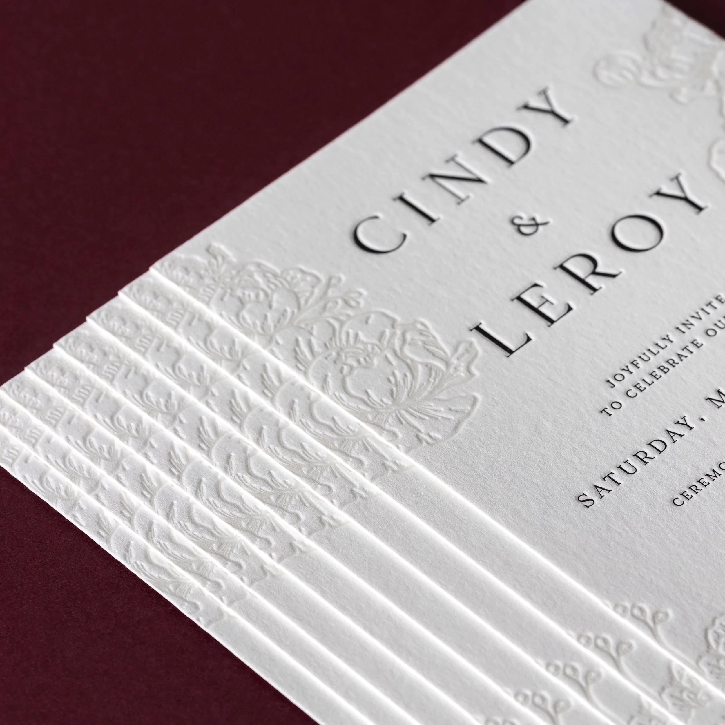 Close-up of a letterpress wedding invitation with deep peony impressions and crisp black typography.