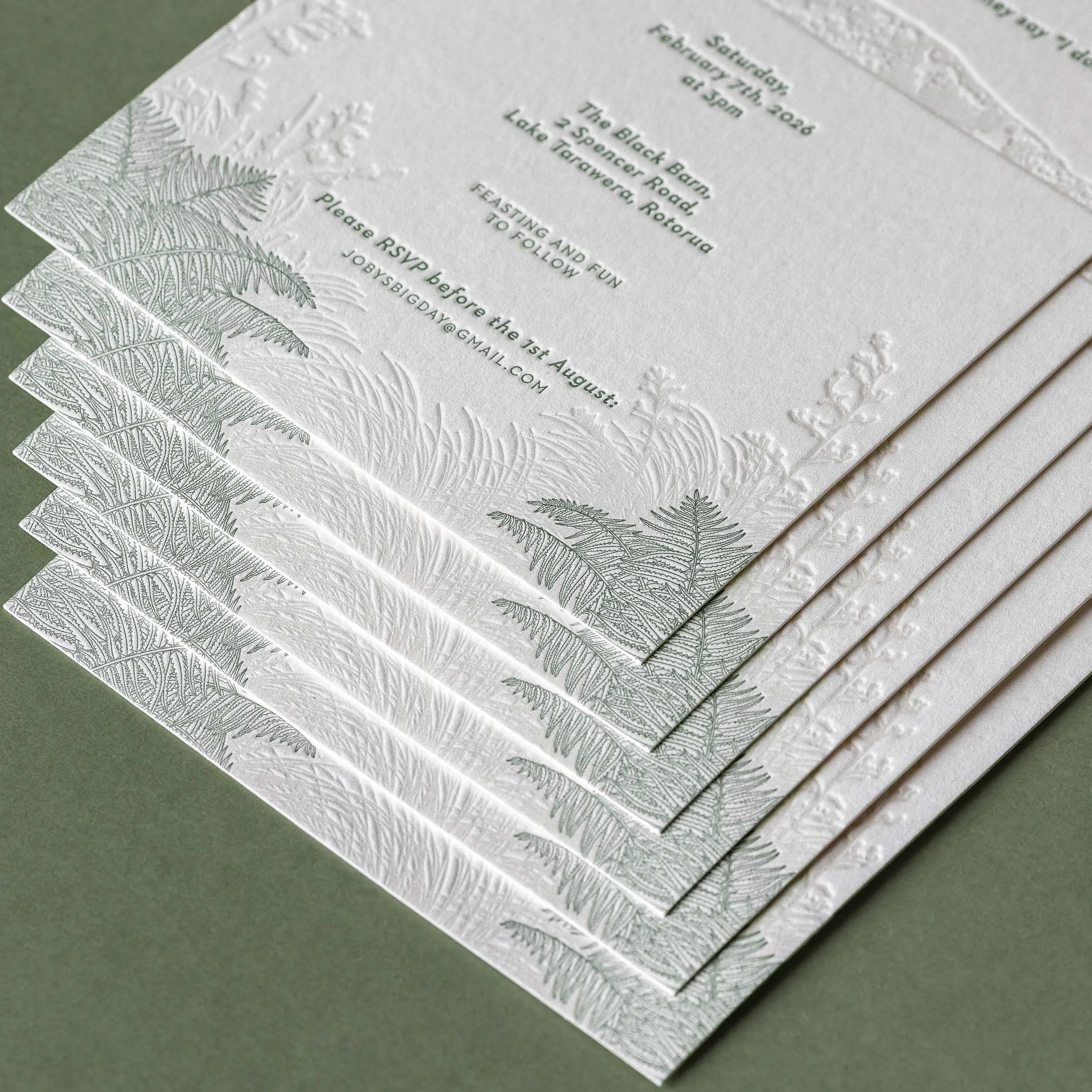 Close-up of a letterpress wedding invitation featuring illustrations of native New Zealand flora including punga fronds and flax.