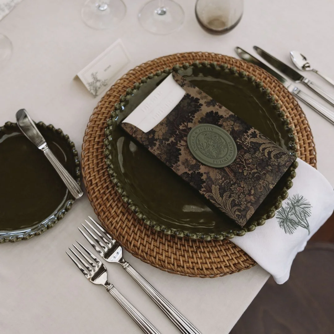 Putiki Estate wedding place setting with tapestry artwork menu, custom wedding crest and embroidered tī kōuka napkin.