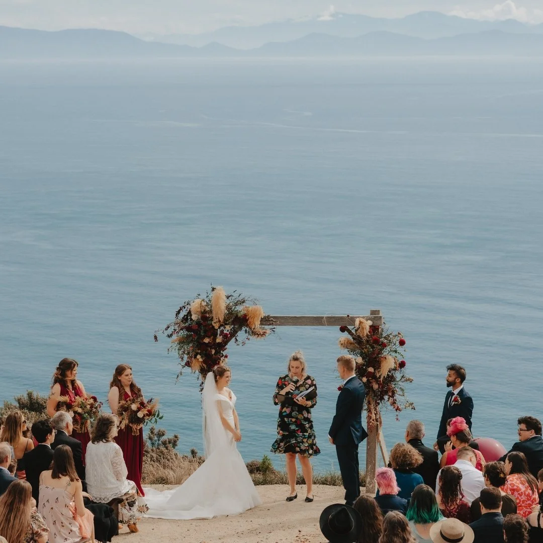 Brontë and Simon’s outdoor wedding ceremony at Boomrock, framed by the floral arch with sweeping ocean views beyond.