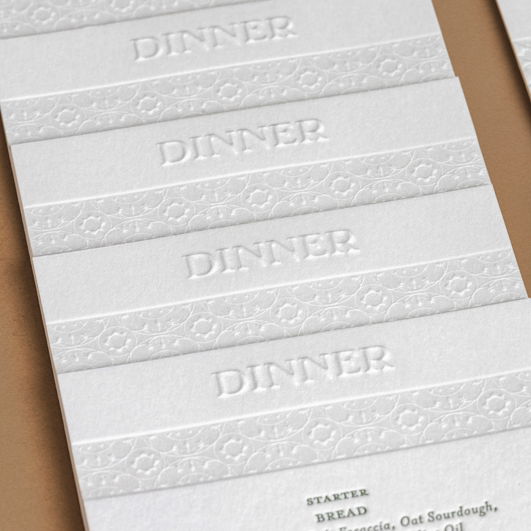 Close-up of wedding dinner menus with embossed headings and letterpress pattern inspired by the tiles at Putiki Estate.