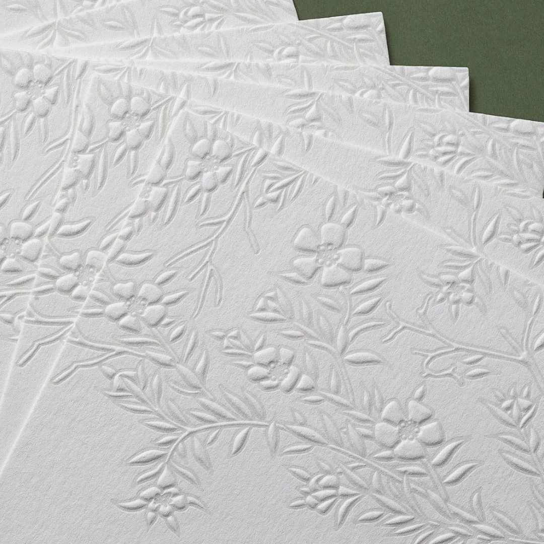 Close-up of detailed mānuka artwork embossed into cream wedding invitation paper.
