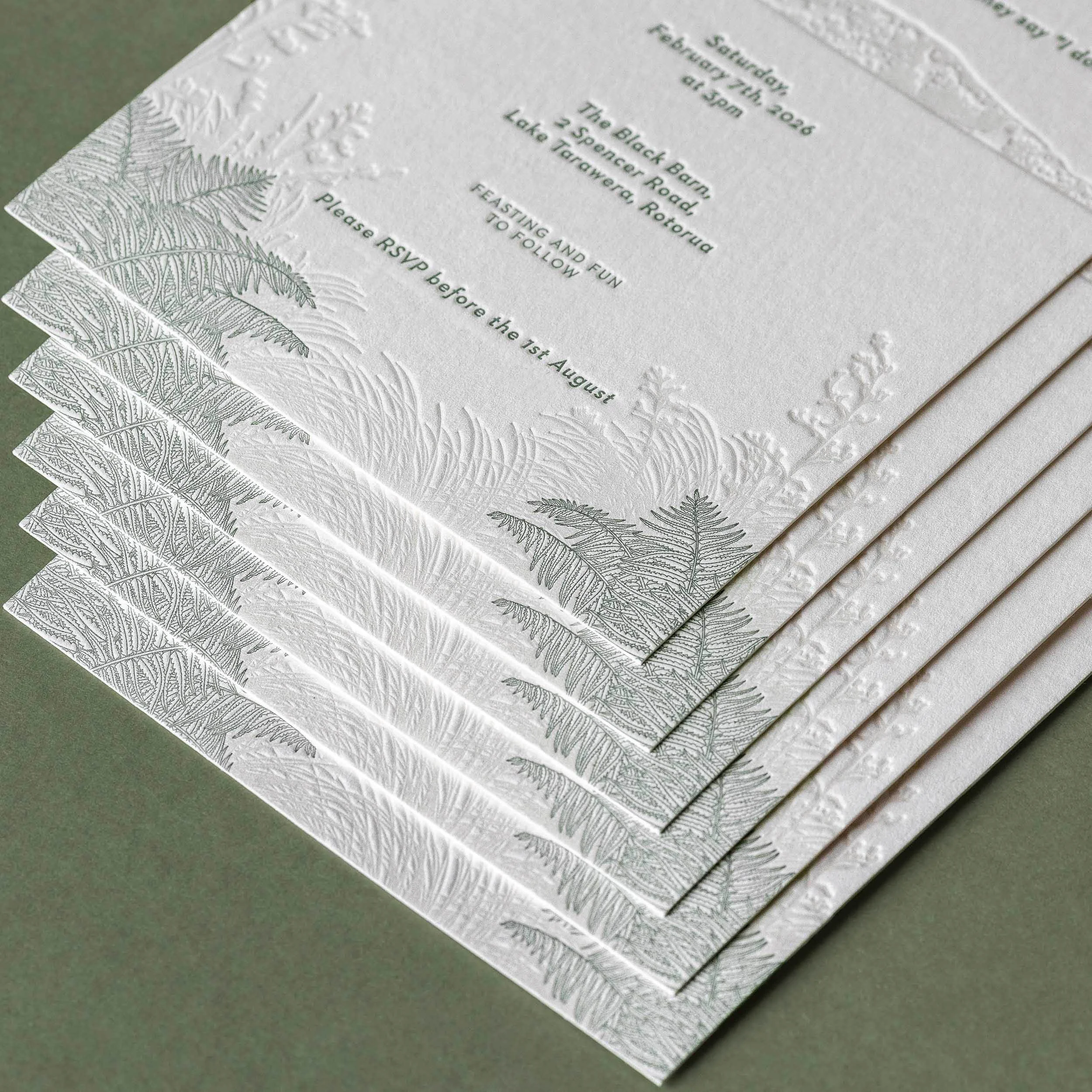 Close-up of a letterpress wedding invitation featuring illustrations of native New Zealand flora including punga fronds and flax.