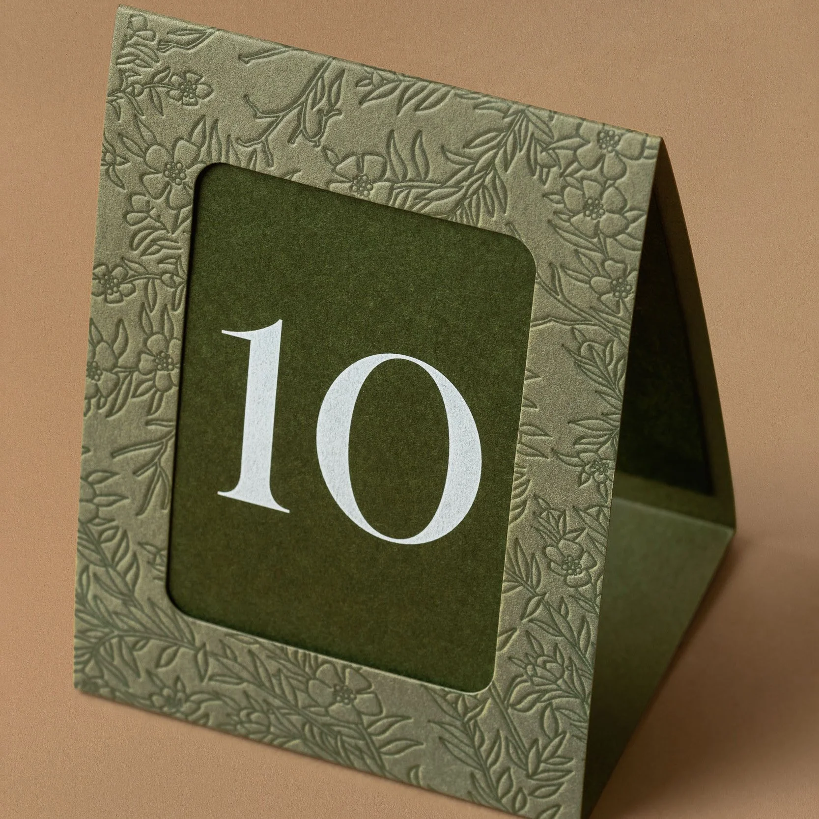 A-frame wedding table number with embossed mānuka frame and white printed number on deep green paper.