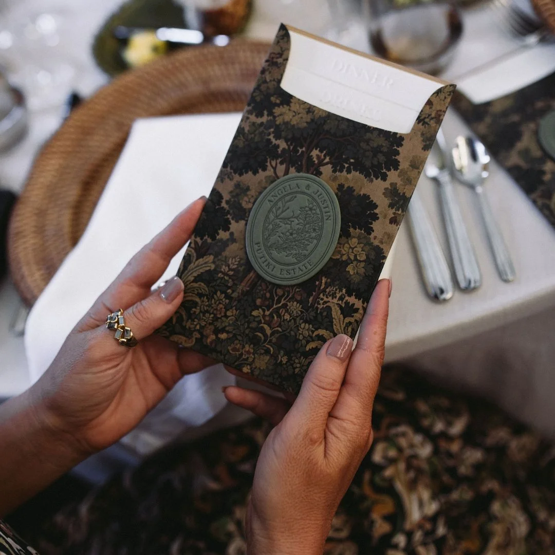 Angela and Justin’s custom dinner and drinks menu at the wedding table, featuring embossed titles and their personalised crest.