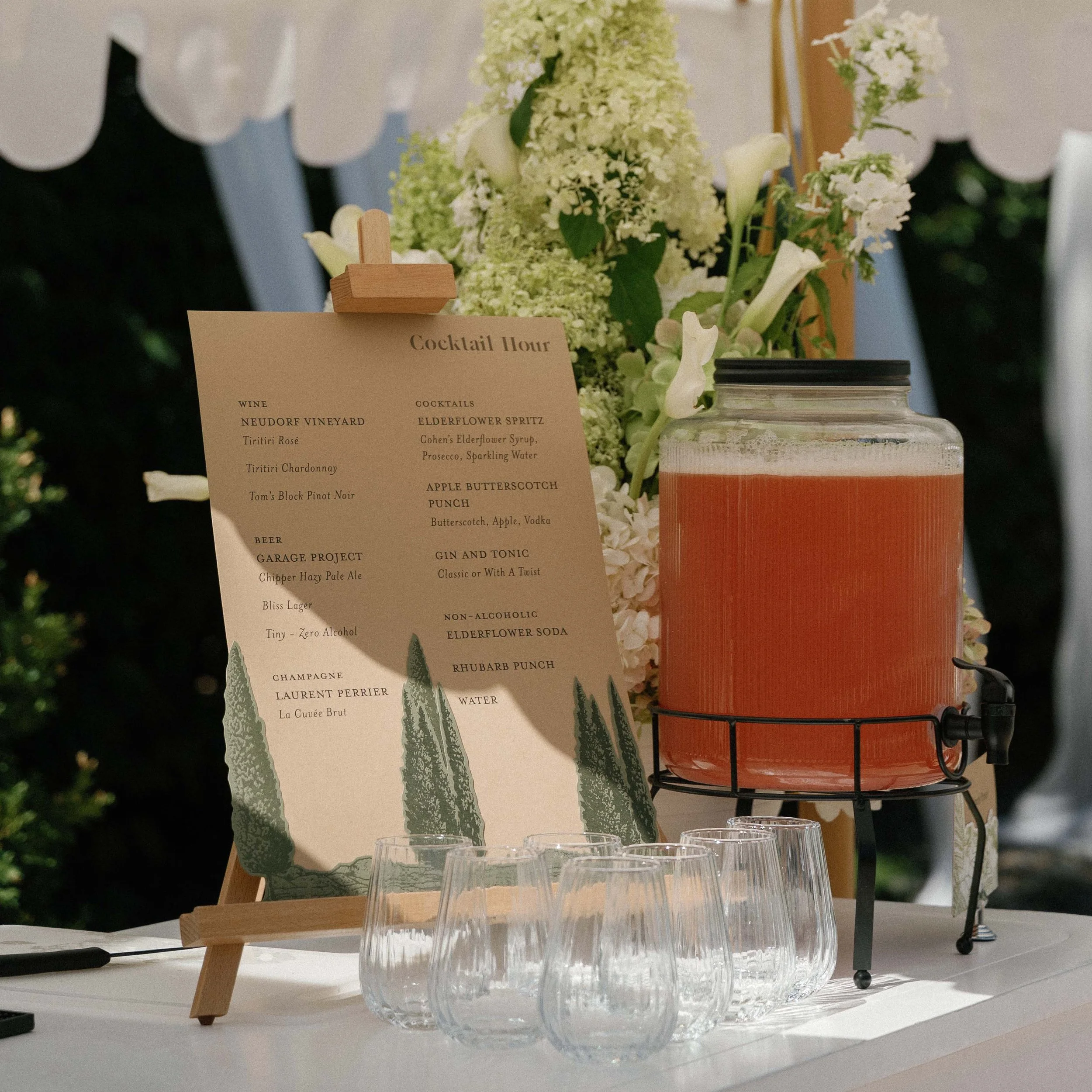 Greer and Cohen’s cocktail hour menu featuring layered die-cut letterpress conifers, displayed beside their homemade rhubarb punch.