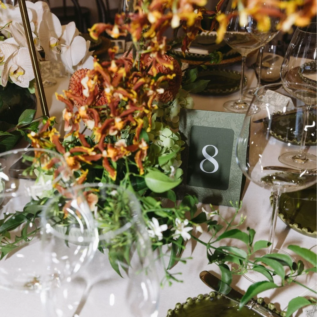 Green table number framed with embossed mānuka artwork among the floral styling at Putiki Estate.
