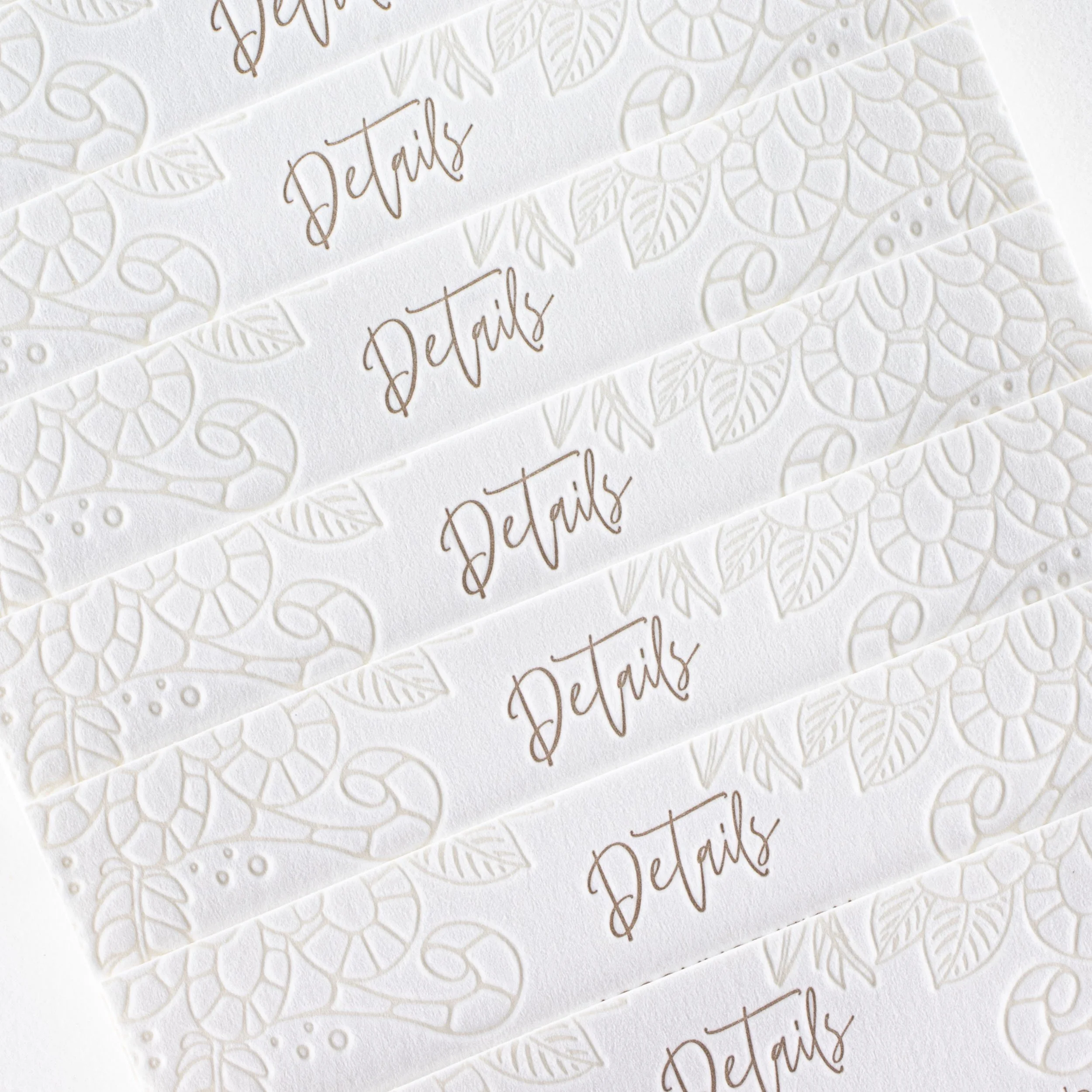 Close-up of Emma and Hayden’s letterpress details cards, showing the deeply impressed floral pattern with warm gold typography.