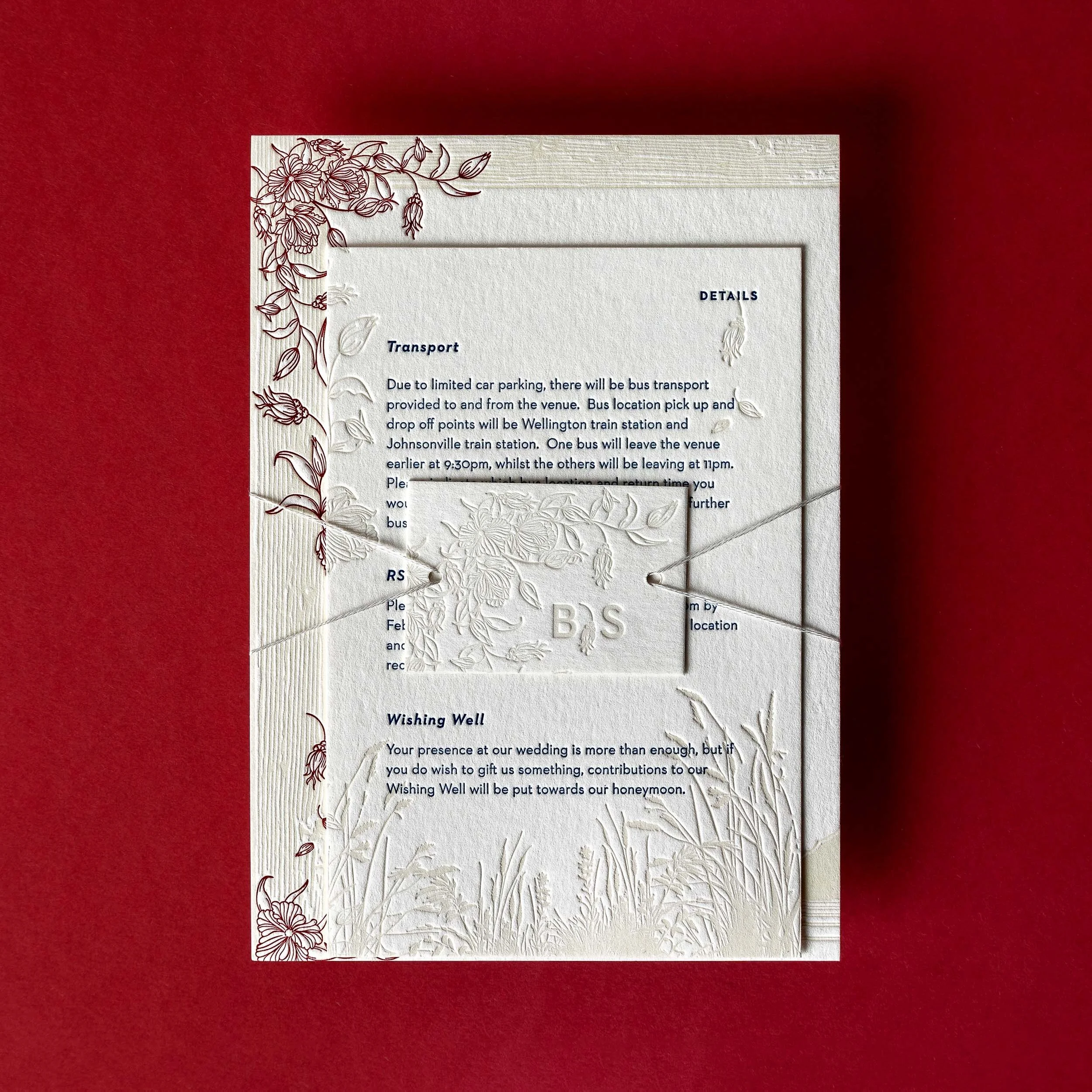 Brontë and Simon’s Boomrock invitation suite, with burgundy floral illustrations aligning across the invitation and details card, finished with a personalised invitation tie.
