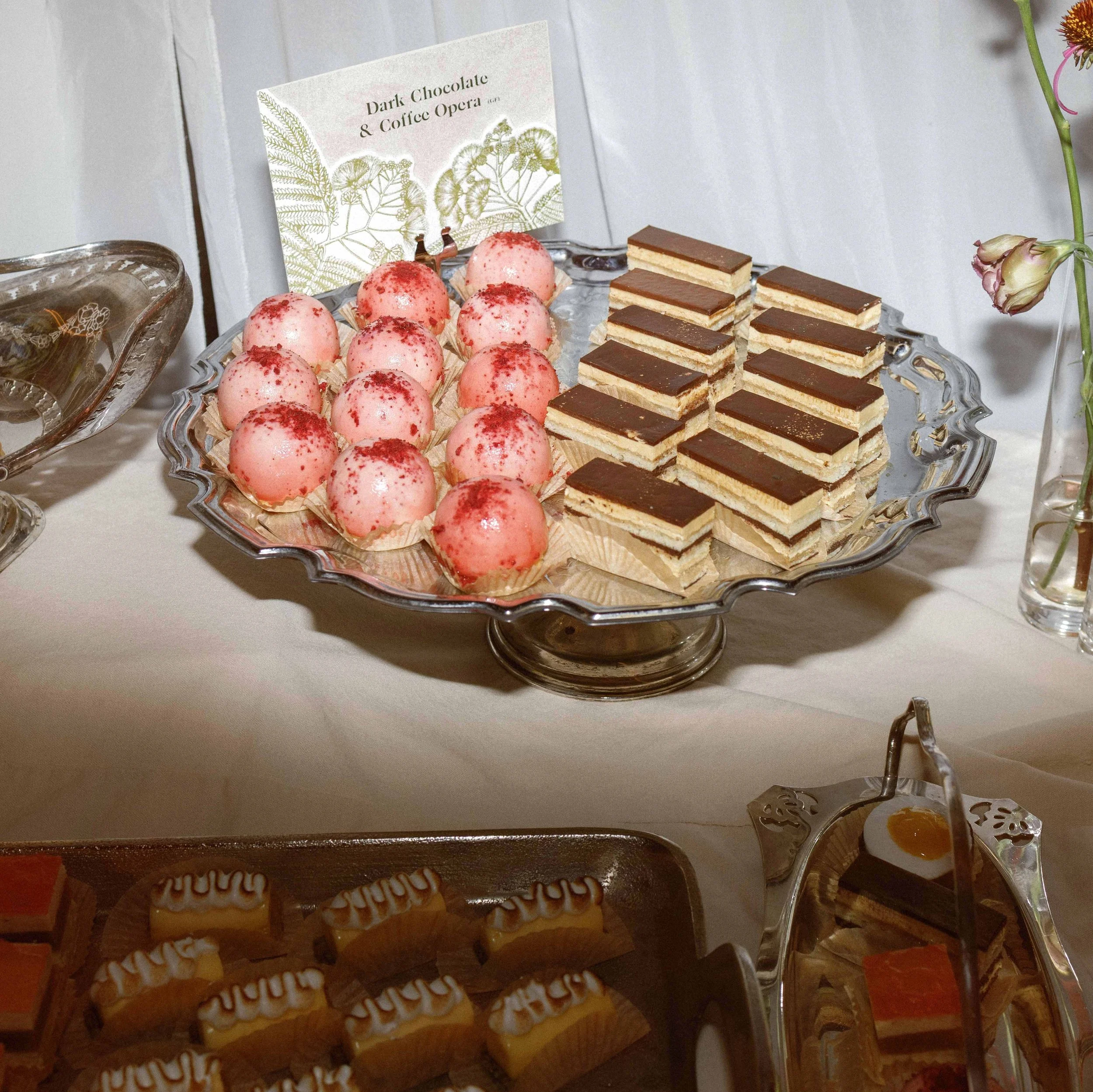 Greer and Cohen’s wedding dessert display with a botanical silk tree flower card identifying the dark chocolate and coffee opera.
