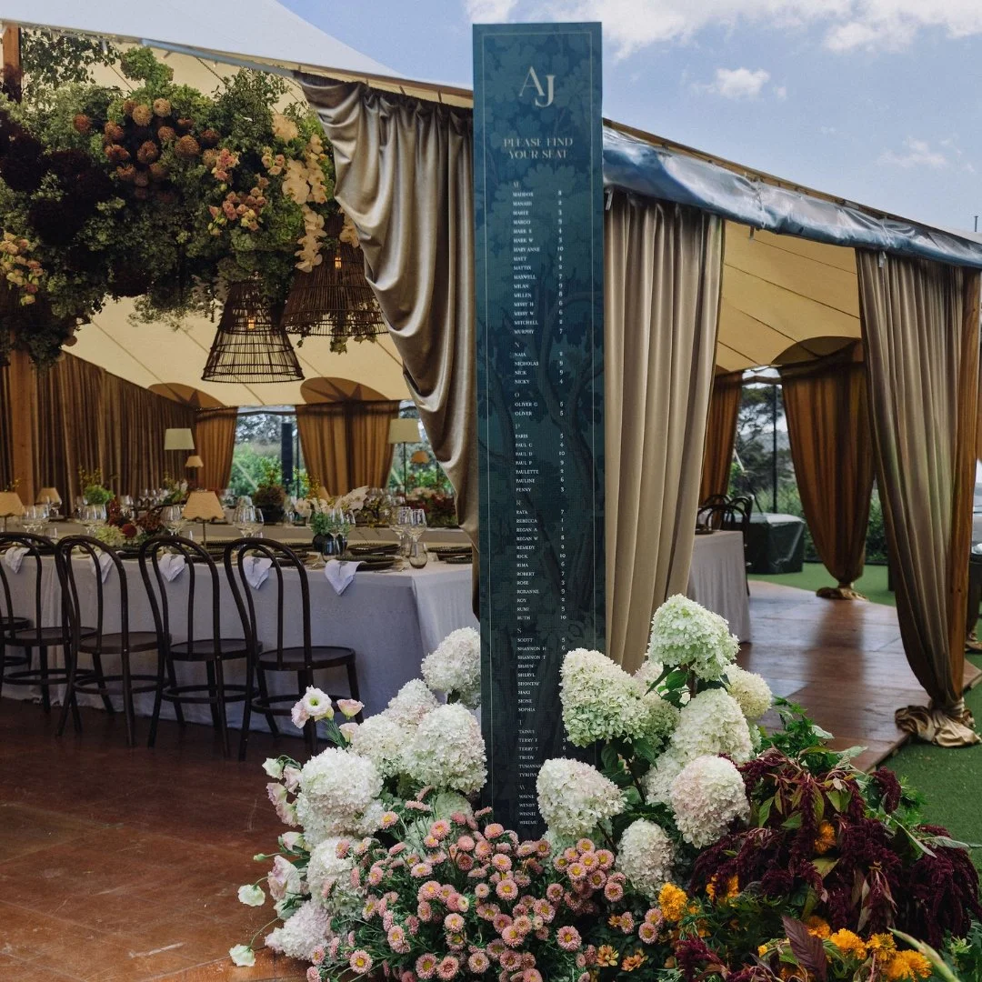 Tall wedding seating plan pillar with tapestry artwork and personalised monogram among the floral styling at Putiki Estate.