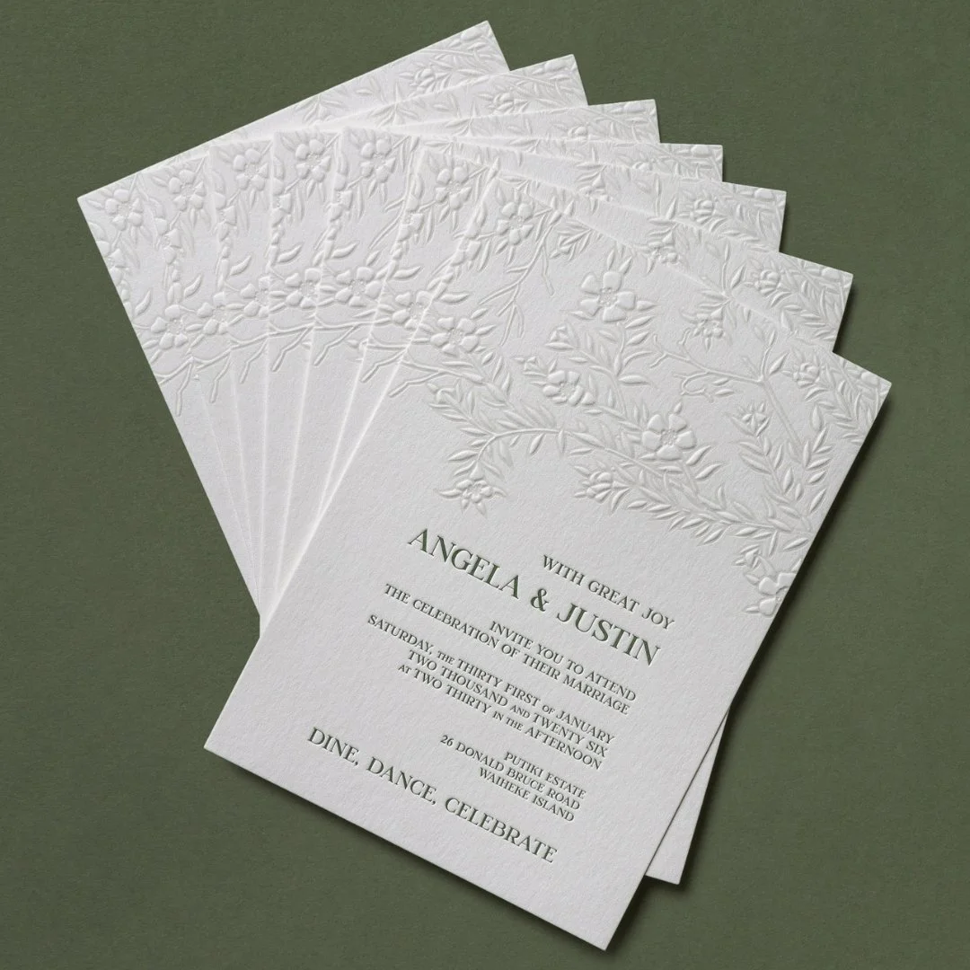 Cream wedding invitations featuring detailed embossed mānuka artwork across the paper.