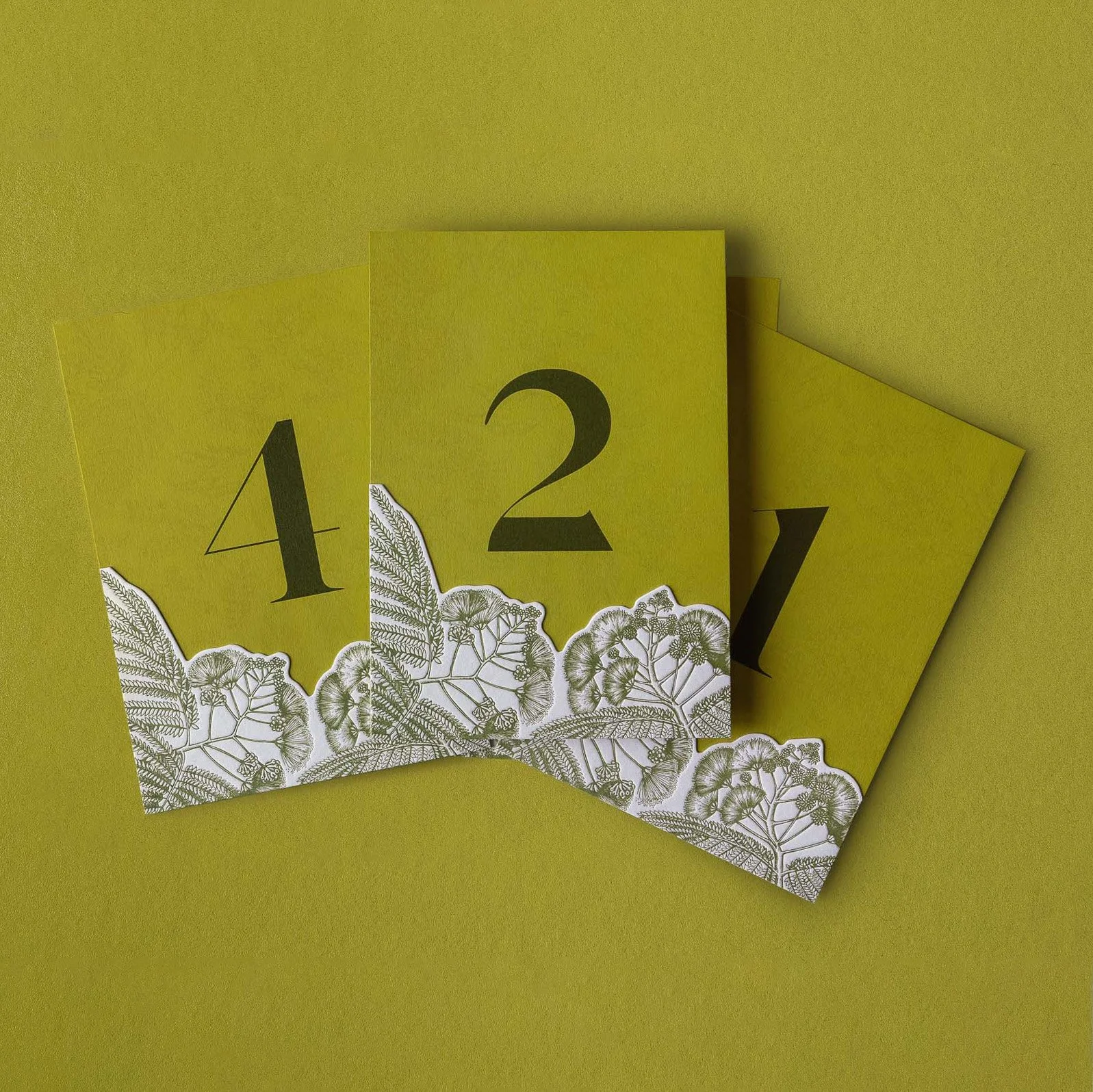 Greer and Cohen’s wedding table numbers featuring layered die-cut silk tree flower illustrations letterpress printed in green.