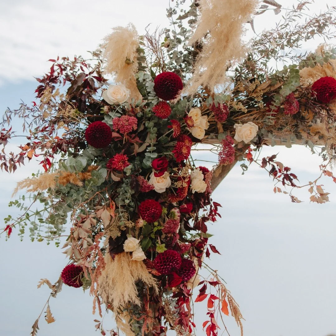 Brontë and Simon’s ceremony arch at Boomrock, decorated with burgundy and cream flowers, foliage and soft dried grasses.