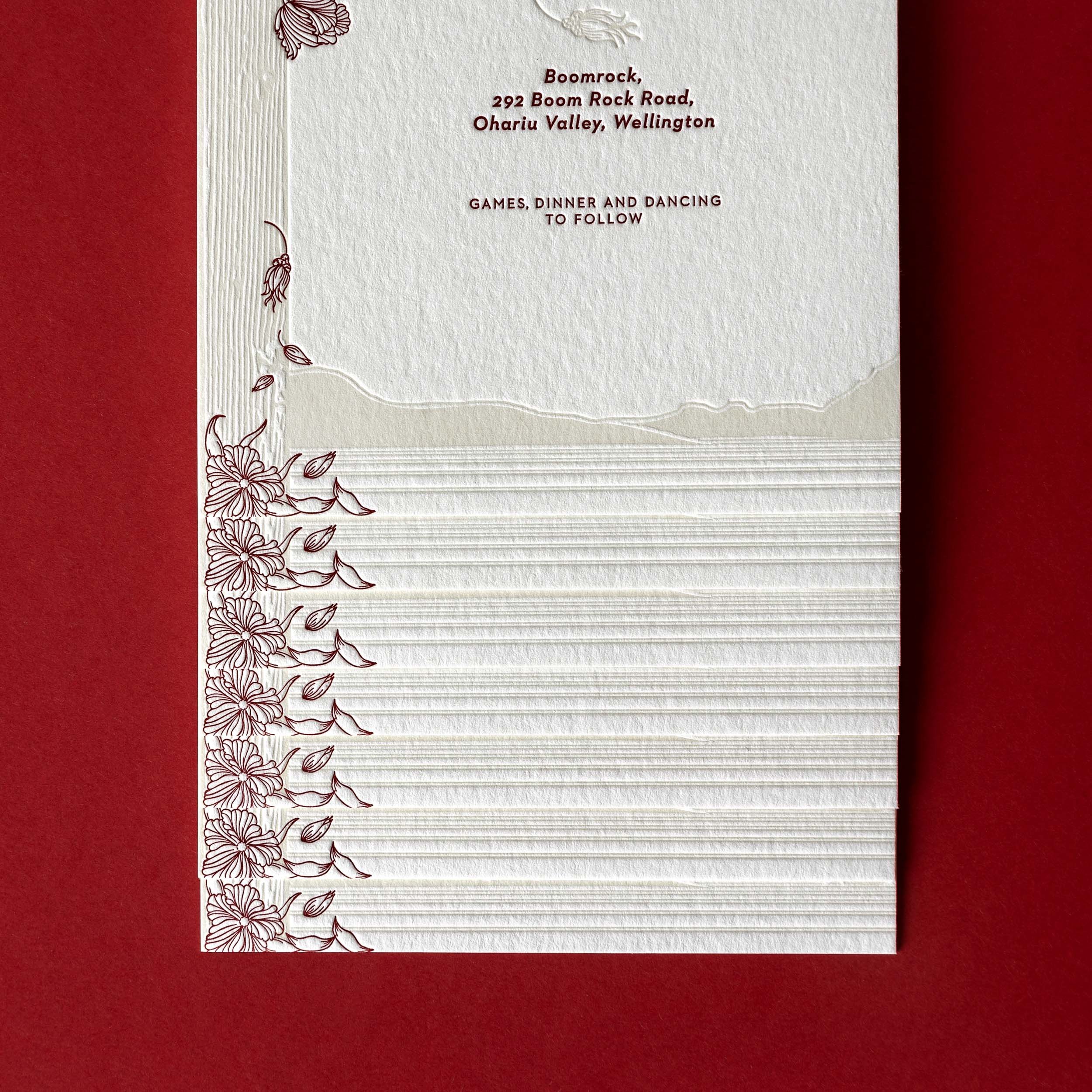 Close-up of Brontë and Simon’s Boomrock wedding invitation, with burgundy florals and a letterpress illustration of the surrounding coastline and cliff tops.