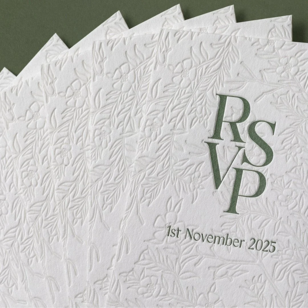 Detail of cream RSVP cards with embossed mānuka artwork and green typography.