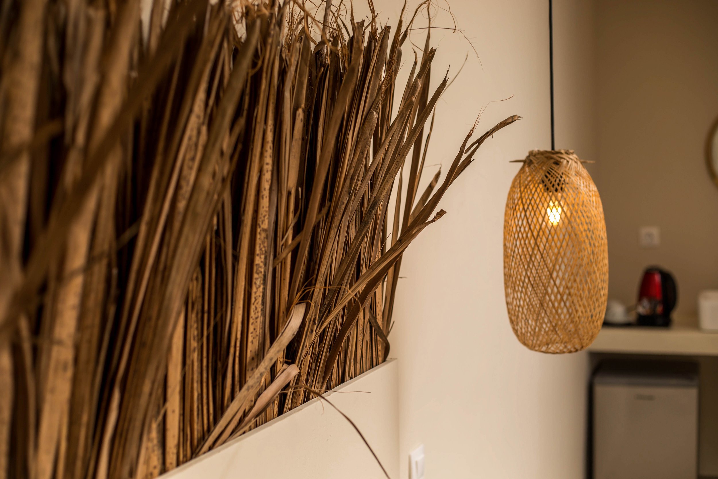 Decorative room scene with a large bundle of dried reeds on the wall and a wicker pendant lamp emitting warm light.