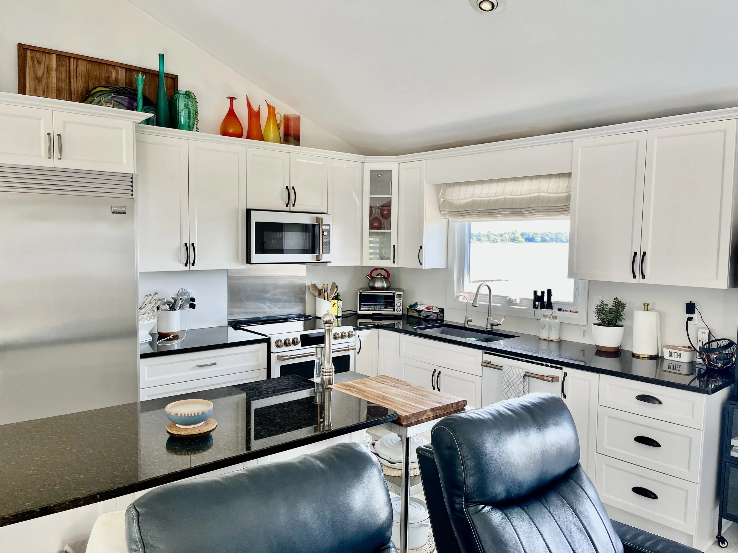 Modern kitchen with white cabinets, black countertops, stainless steel appliances, and a window overlooking a body of water.
