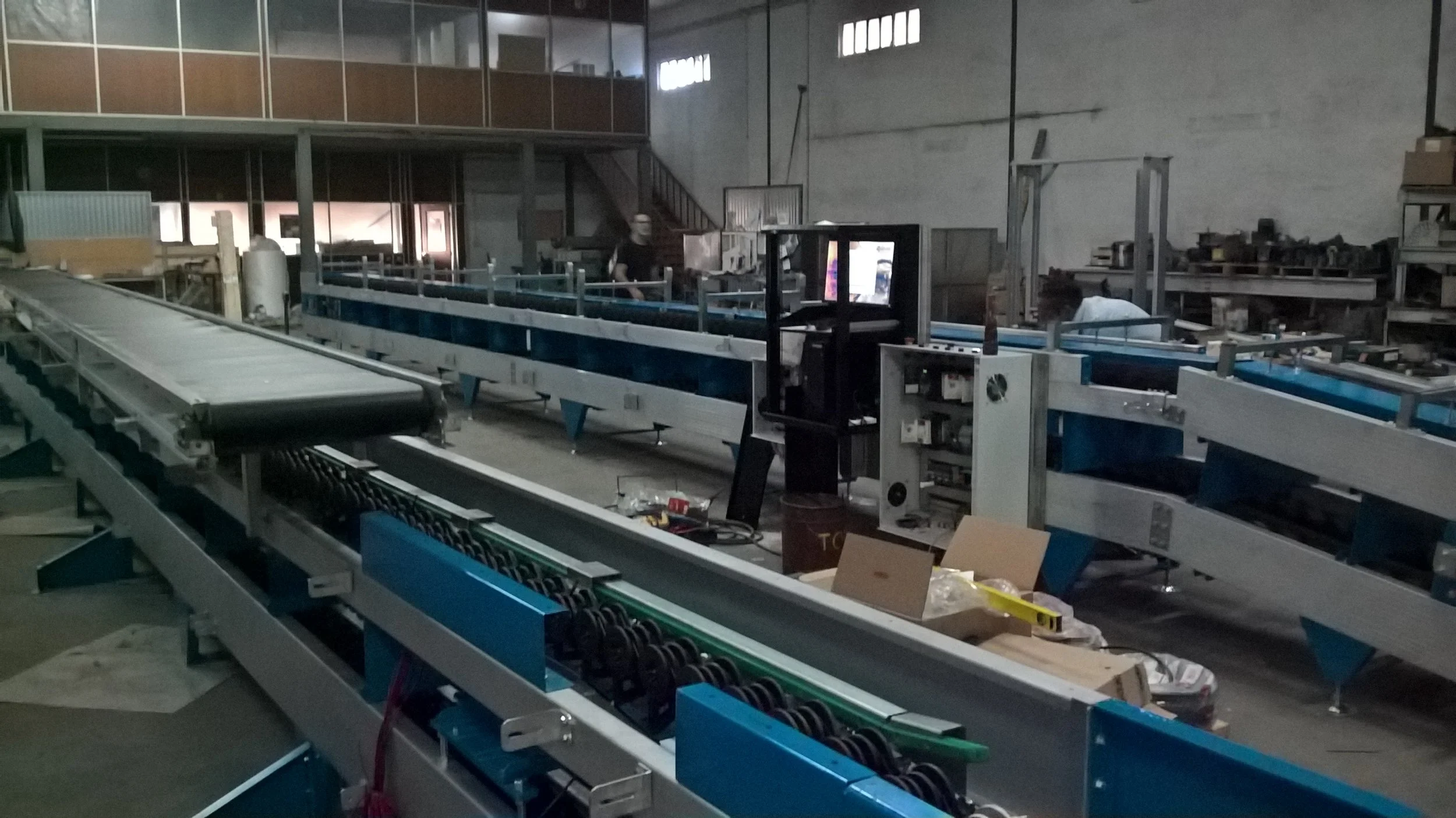 Interior de uma fábrica com máquinas industriais e uma pessoa trabalhando ao fundo.