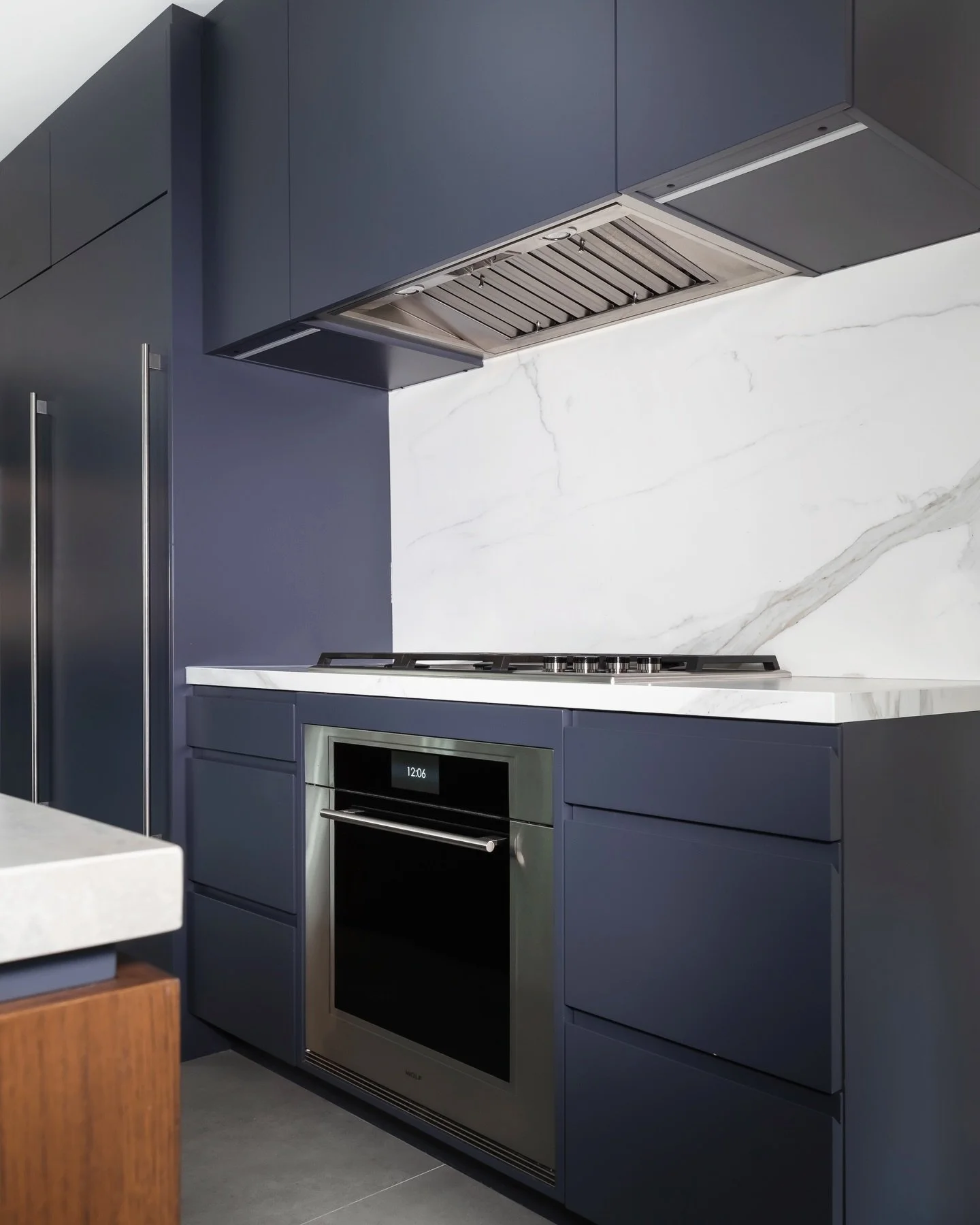 The kitchen at Project Douglas is rooted in simplicity and proportion. Deep-toned cabinetry anchors the room, allowing the architecture and materials to speak first. A monolithic island, softened by a concrete-like finish, becomes the natural gatheri