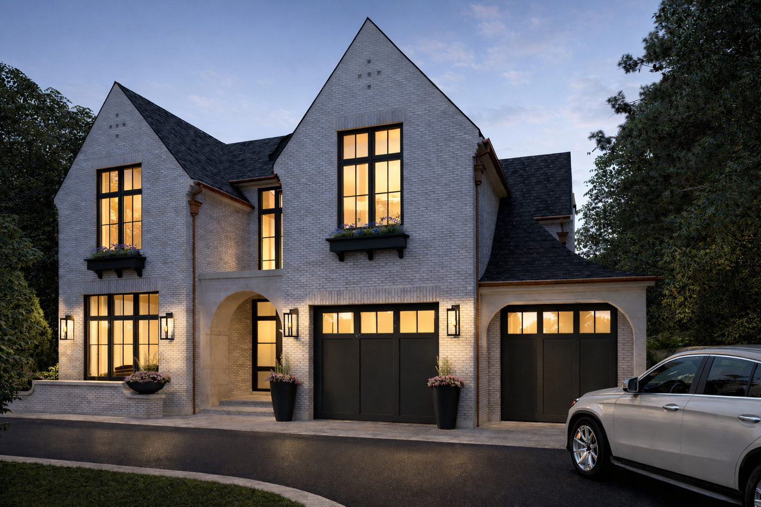 Modern two-story house with white brick exterior, large illuminated windows, black garage doors, landscaped planters, and a silver car parked outside during dusk.