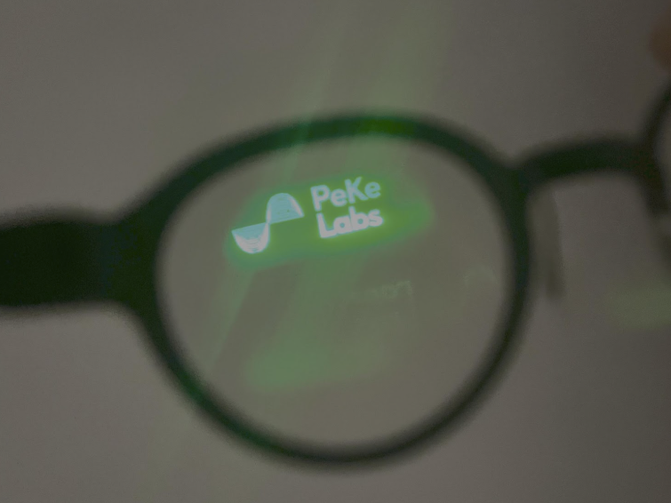 The image shows a pair of glasses with a green glow reflection of the logo 'Peke Labs' with a pipe icon.