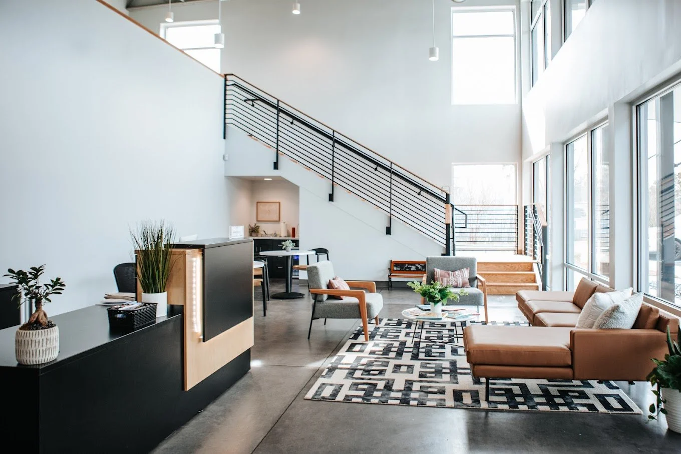 Interior view of a modern reception area with staircase, cozy seating, and stylish decor. Combines industrial elements with warmth—ideal for a creative or community-based facility.