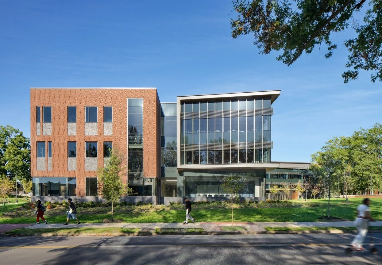Exterior courtyard of a curved, glass-wrapped building surrounded by landscaped greenery and blossoming trees. Emphasizes harmony between architecture and nature, promoting open space and natural light.
