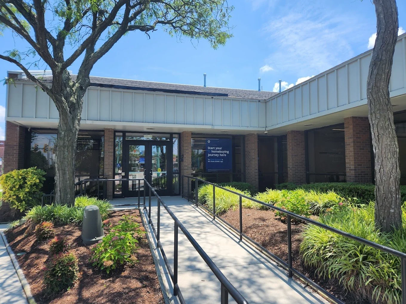 Main entrance to a Chase bank branch featuring a ramp for accessibility, landscaped walkway, and glass double doors. Emphasizes inclusive design and a welcoming customer experience.
