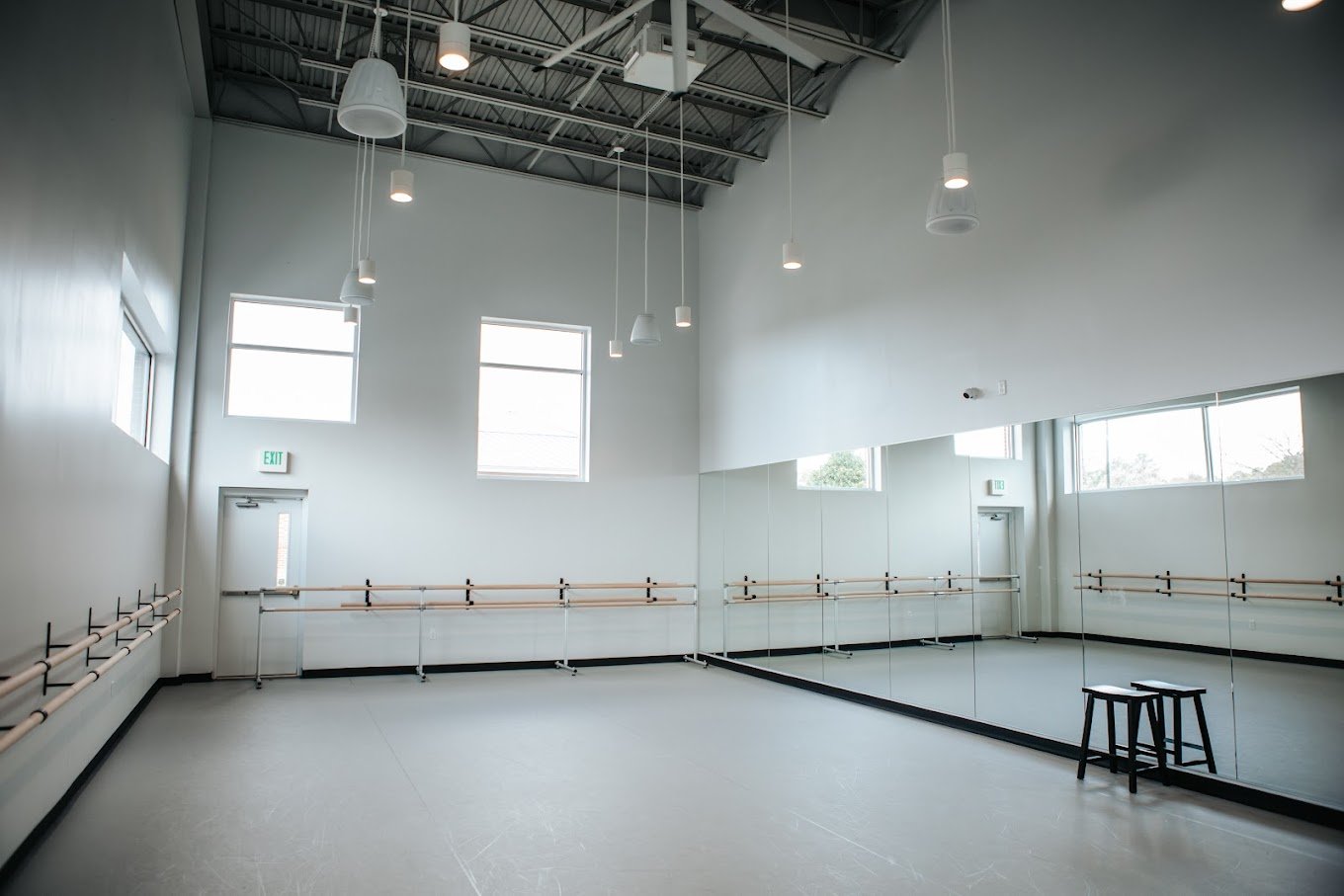 Another angle of the dance studio with resilient flooring, mirrored wall, ballet barres, and soft natural lighting. Emphasizes flexibility for dance, fitness, or rehearsal use.