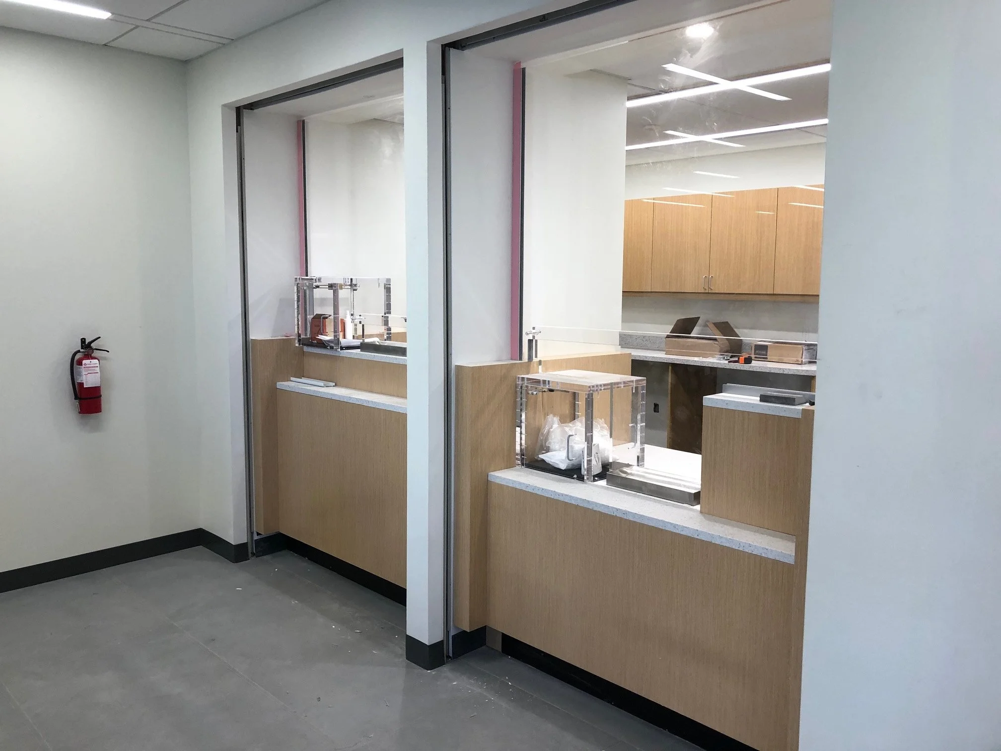 Interior construction view of teller windows being installed, with wood paneling and transparent security barriers. Highlights progress in branch renovation and modern banking infrastructure.