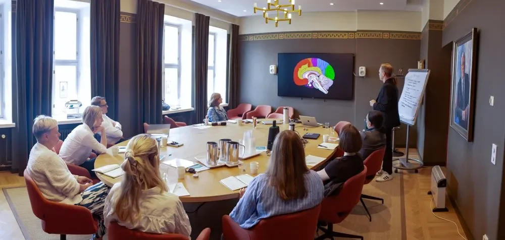 Yritystapaaminen neuvotteluhuoneessa, jossa seurataan esitystä valkokankaalla, istuu seitsemän ihmistä ja yksi esittelijä.