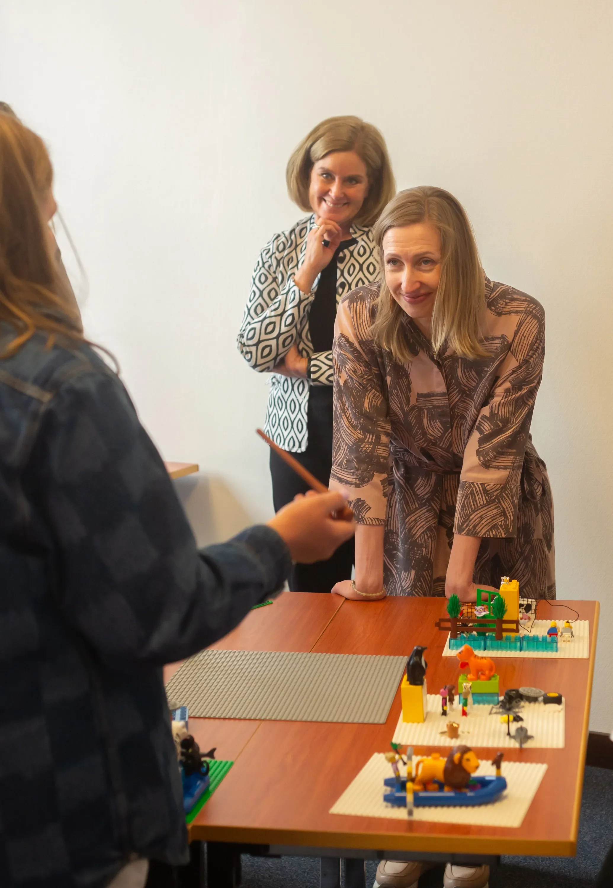 Nainen katsomassa Lego-rakennelmaista kappaletta pöydällä, toinen nainen seisoo taustalla, ohikulkija keskustelussa