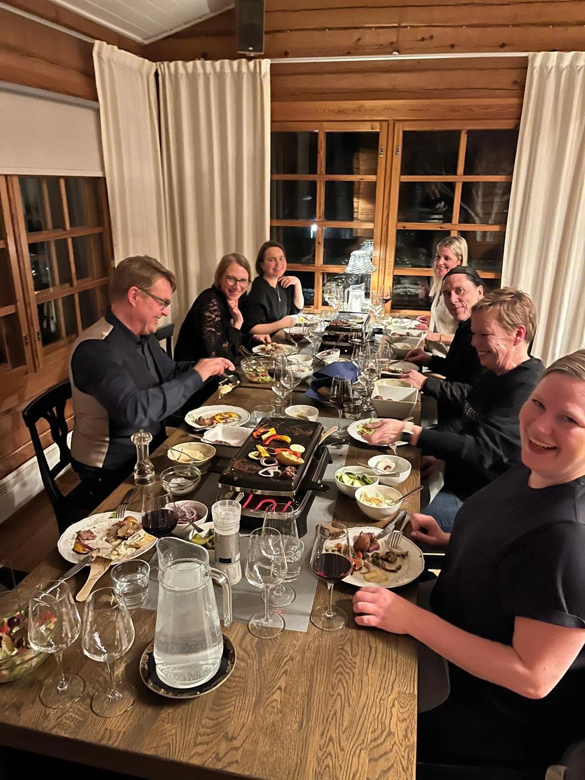 Illallinen pöydässä, jossa on paljon ruokaa ja juomia, ihmiset nauttivat yhteisestä hetkestä.